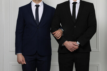 Gay couple in elegant suits standing near white wall, closeup