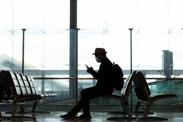 silhouette of young travel backpack using smartphone in the Passenger Departure Arrival building in the airport. He travel alone in station.
