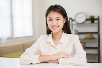 Obraz premium Young asian woman looking at camera video conference online sitting in living room at home. Business Woman looking at screen Meeting on social media live steam. Work, learning from home.
