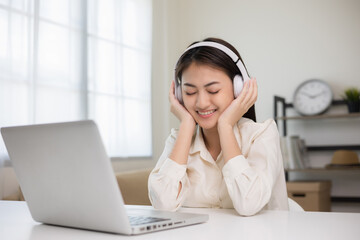 Naklejka premium Young asian woman in headphone using laptop chatting video conference online sitting in living room at home. Business Woman look at screen Meeting on social live steam. Work, learning from home.