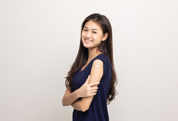 Obraz premium Vaccination. Young beautiful asian woman getting a vaccine protection the coronavirus. Smiling happy female showing arm with bandage after receiving vaccination. On isolated white background.