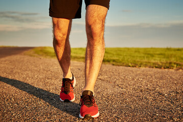 Male runner feet on road at sunset, close up. Sport sneakers for jogging. Fitness and healthy lifestyle concept