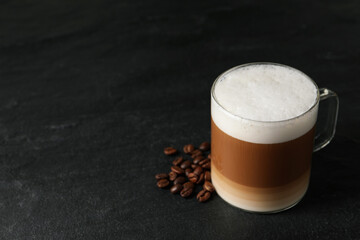 Glass cup of delicious layered coffee and beans on black table, space for text