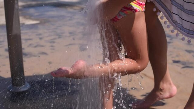 Woman's hand washes little cute legs feet of child under running water. In summer, beach always an opportunity wash yourself from sand and salty sea water. Comfortable rest.