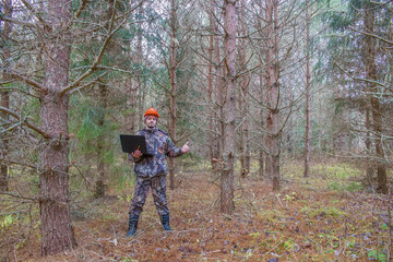 Forest engineer works in the forest with a computer. An ecologist in a young forest holds a computer in his hands.