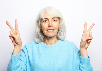 Good mood happy smiling positive elderly woman with white hair, wearing blue sweater show v-sign.