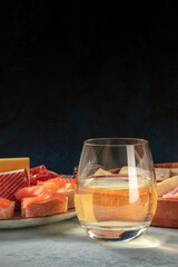 A glass of white wine with salmon sandwiches and cheese, a side view on a dark background with copy space. Elegant Spanish tapas in a bar