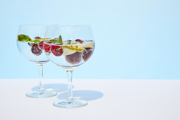 Cool sparkling water, lemonade, water, cocktail with fresh cherries and mint leaves stands on a pastel blue background. Summer refreshing drinks concept