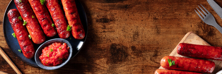 Sausages with ketchup panorama, overhead flat lay shot on a dark rustic wooden background with a...