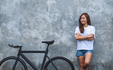 Fototapeta na wymiar Portrait image of a beautiful young asian woman wearing white t-shirt and jean short pant with bicycle and concrete wall background