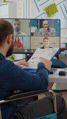 Back view of handicapped paralysed invalid manager talking with team on videocall about sale...
