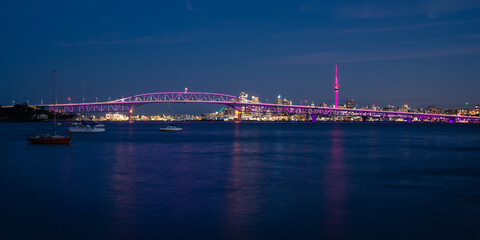 Obraz premium Auckland Sky Tower illuminated in pink and Harbour Bridge in purple