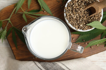 Obraz na płótnie Canvas Glass jug with fresh hemp milk, seeds and leaves on wooden board, flat lay
