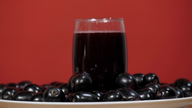 A few Indian blackberries falling on a heap of fruits kept together on a plate. Indian summer fruit. Traditional Kala Jamun juice / beverage kept in a clear glass against a colored background - a c...