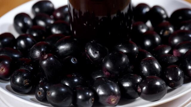 Popular Indian Java plum fruit kept on a white plate rotating on a turntable. Indian summer fruit. Human hand keeping a glass of freshly made Indian blackberry juice with its fruits in the middle o...