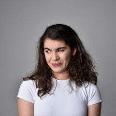 Fototapeta premium Close up portrait of young woman with natural brown hair, over the top facial expressions on light grey studio background.
