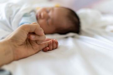 The baby's hand holds the mother's finger while sleeping. Relationship and love of mother and child