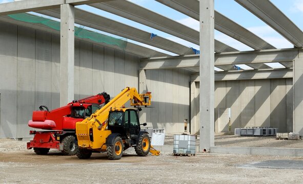 Back of two telescopic handlers inside a concrete block building under construction.