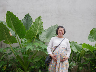 Portrait of Asian pregnant woman standing on green nature background, looking at camera