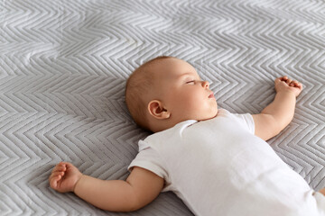 Cute newborn baby wearing white bodysuit lying on bed on grey blanket, charming baby relaxing at...
