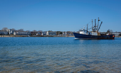 Fototapeta premium Commercial fishing boat sailing on blue sea water canal to the left. Peaceful seascape of the maritime village with ship passing on a bright summer day.