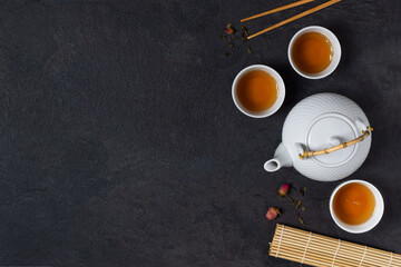 Teapot and tea cups with tea drink top view on black background.