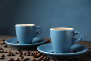 Cups of tasty espresso and scattered coffee beans on wooden table