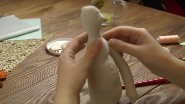 Human hands make rag doll on wooden table. Process of making toys from natural linen fabric. Handmade diy work.