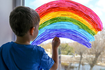 Child at home draws a rainbow on the window. Flash mob society community on self-isolation...