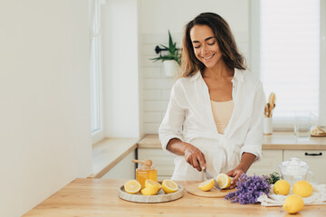 Young woman making lemonade in a kitchen of cozy house. Homemade healthy drink.