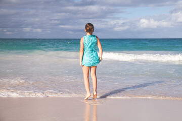 Little girl in a blue dress stands on a beach.