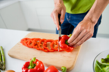 Cropped photo young man cooking breakfast slicing red paprika with knife