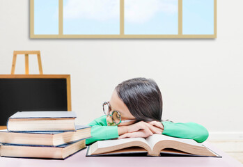 Asian little girl with eyeglasses lying on the book on the table