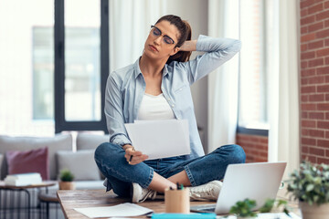 Smart business woman with neck pain looking uncomfortable while working with laptop sitting on the...