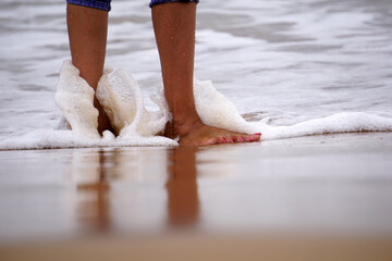 female foot touching water wave at sea beach