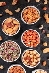 Many different nuts in bowls, shot from the top on a black slate background