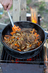 cooking pilaf in a cauldron on a campfire roasting meat, onions and carrots