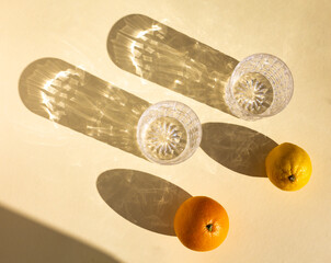 top view of a pair of empty crystal glasses, orange and lemon under hard sunlight, glitter...