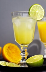 a vintage goblet of refreshing citrus lemonade or alcoholic cocktail on grey background closeup, cutting lime, lemon and orange are around the glass of citrus ice drink