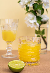 a crystal glass with a refreshing citrus drink or lemonade or alcoholic cocktail on beige flower background, minimalistic pastel still life