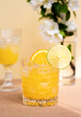 a crystal glass with a refreshing citrus drink or lemonade or alcoholic cocktail decorated with sliced lime and orange on beige flower background closeup,  minimalistic pastel still life