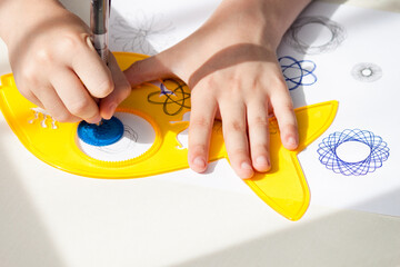 child drawing spirograph pattern with spirograph kit, flat lay.