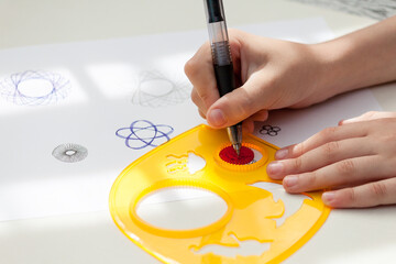 child drawing spirograph pattern with spirograph kit, flat lay.