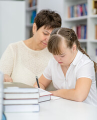 Old teacher helps to girl with syndrome doing homework at library. Education for disabled children concept