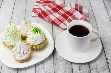 Cupcake with cream, white cup with tea, cotton napkin on a light wooden background. The concept of breakfast, afternoon tea, sweet food. Top and side view. Selective focus.