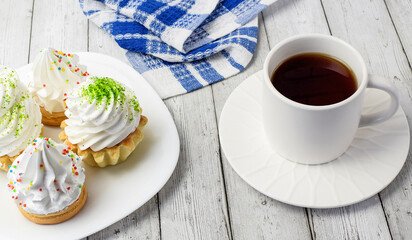 Cupcake with cream, white cup with tea, cotton napkin on a light wooden background. The concept of breakfast, afternoon tea, sweet food. Top and side view. Selective focus.