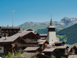 View of traditional wooden houses, also called Swiss chalet, and the church tower in the village of Grimentz, in the canton of Valais (Switzerland), municipality of Anniviers. Alps in the background.