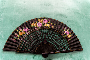 Black fan decorated with flowers on a wooden background painted in turquoise green.