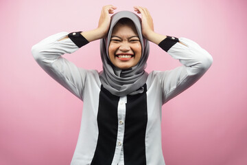 Beautiful young asian muslim woman shocked, dizzy, stressed, unhappy, many problems, want solution, with hands holding head isolated on pink background