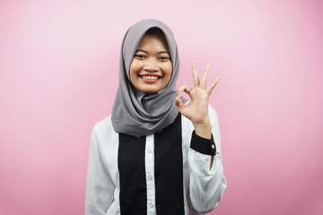 Beautiful young asian muslim woman smiling confident, enthusiastic and cheerful with hands ok sign, success, good job, success sign, isolated on pink background
